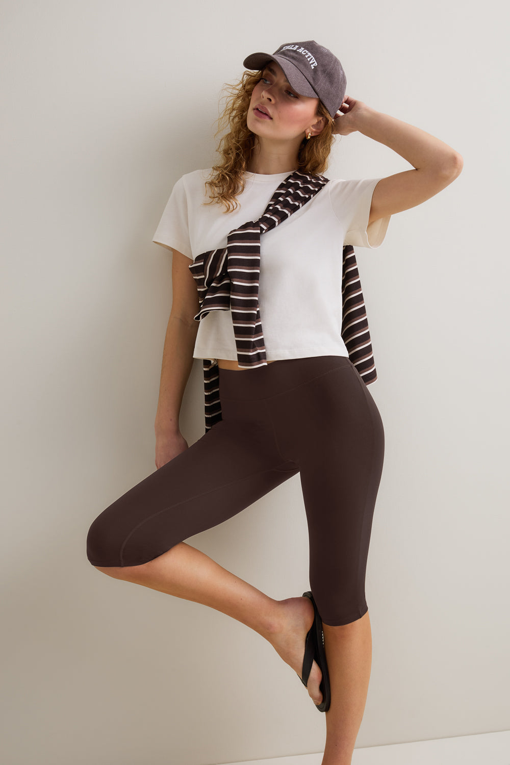 Woman wearing a white t-shirt, brown capri pants, and a striped scarf against a plain background
